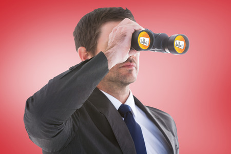 Young businessman looking through binoculars against red vignetteの写真素材