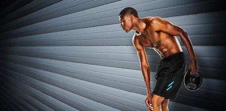 Shirtless fit young man holding barbell weight against grey shutters