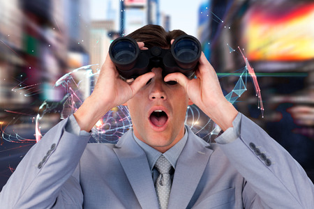 Suprised businessman looking through binoculars against global technology background in blueの写真素材