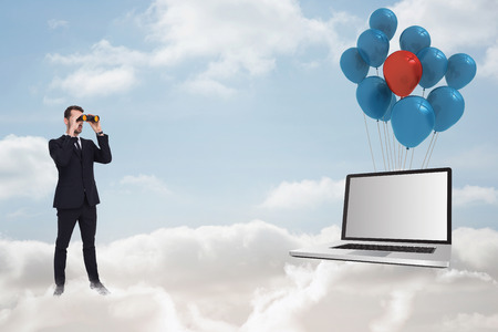 Elegant businessman standing and using binoculars  against cloudy skyの写真素材