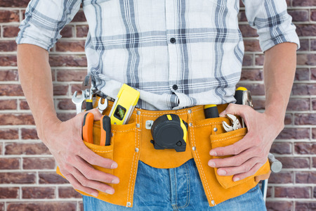 Cropped image of technician with tool belt around waist against red brick wallの写真素材
