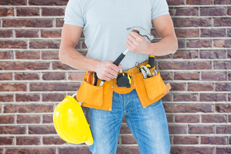 Worker holding hammer over white background against red brick wall