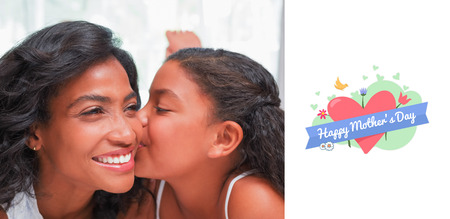 mothers day greeting against pretty woman lying on bed with her daughter kissing cheekの写真素材