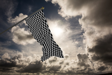 Checkered flag against dark sky with white cloudsの写真素材