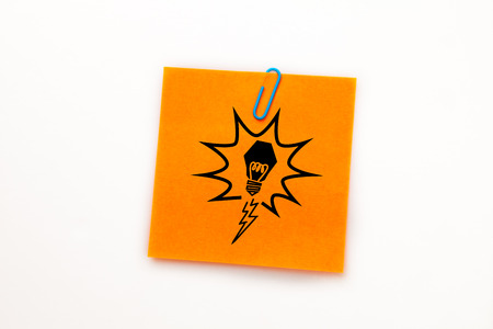 Light bulb against orange adhesive note with a paperclip