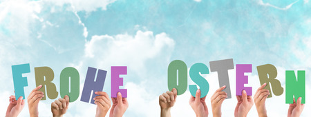 Hands holding up frohe ostern against blue skyの写真素材