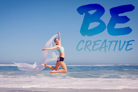 Fit woman jumping gracefully on the beach with scarf against be creative