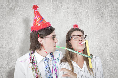 Geeky hipster wearing a party hat with blowing party horn against white backgroundの写真素材