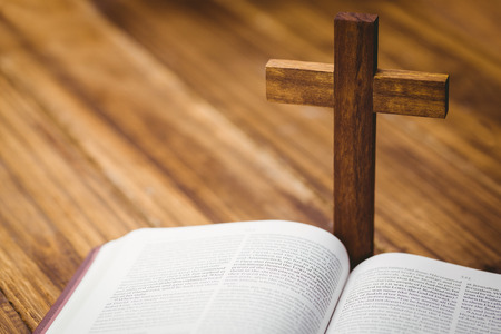 Open bible with crucifix icon behind on wooden tableの写真素材