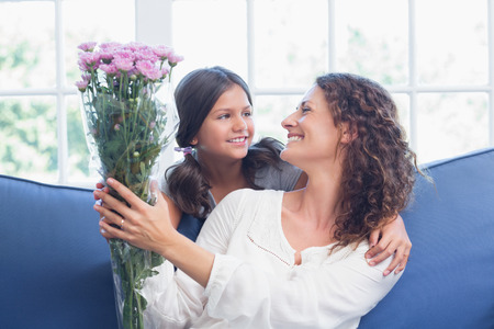 Happy mother and daughter sitting on the couch with flowers in the living roomの写真素材