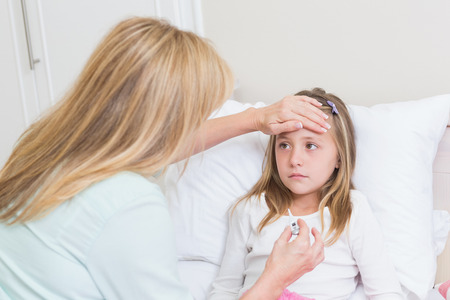 Mother measuring her daughters temperature in the bed roomの写真素材