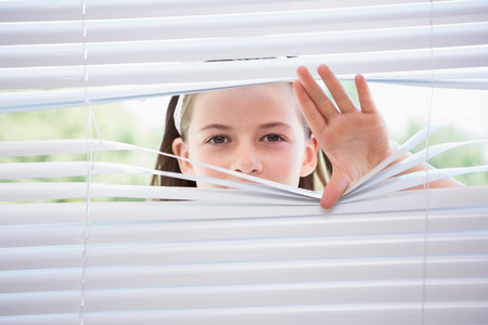 Little girl peeking through blinds from outsideの写真素材