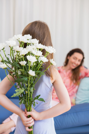 Daughter surprising mother with flowers at home in the living roomの写真素材