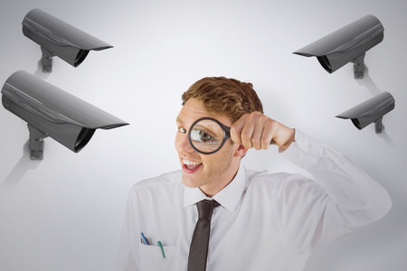 Geeky businessman looking through magnifying glass against cctv cameraの写真素材