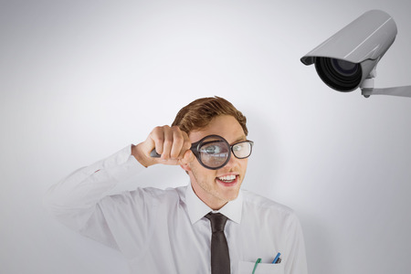 Geeky businessman looking through magnifying glass against cctv cameraの写真素材