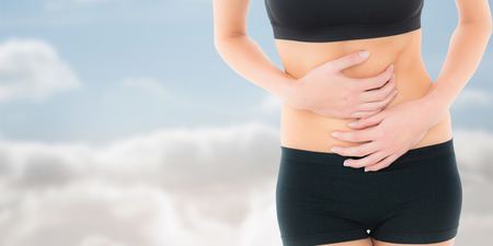 Mid section of a fit young woman with stomach pain against cloudy skyの写真素材