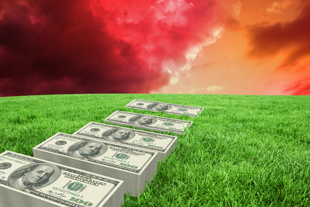 Stacks of dollars against green grass under red and purple skyの写真素材