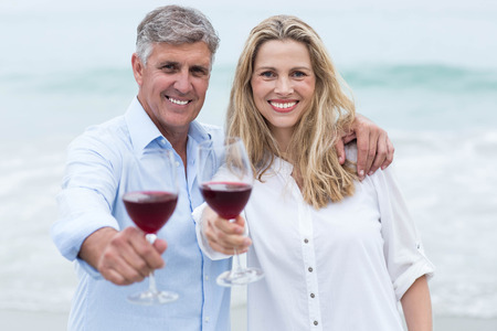 Happy couple smiling at camera and toasting at the beachの写真素材