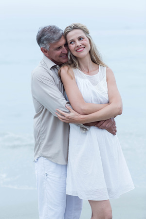 Happy couple standing by the sea and hugging each other at the beachの写真素材