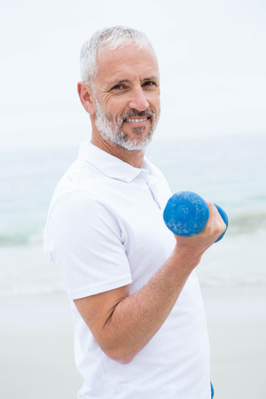 Fit man lifting dumbbells at the beachの写真素材