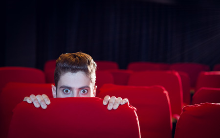 Young man watching a scary film at the cinemaの写真素材