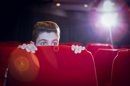 Young man watching a scary film at the cinema