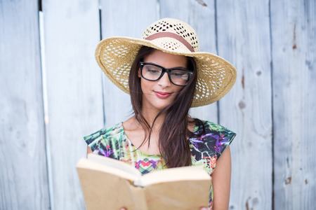 Smiling beautiful brunette reading a book on wooden plank backgroundの写真素材