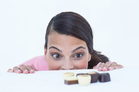 Pretty brunette peeking at chocolate on white backgroundの写真素材
