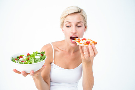 Pretty woman deciding eating pizza rather the salad on white backgroundの写真素材