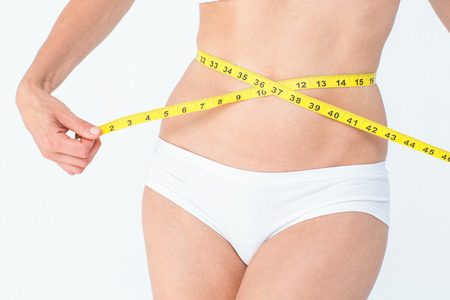Attractive woman measuring her belly on white backgroundの写真素材