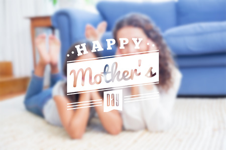 mothers day greeting against happy mother and daughter lying on the floorの写真素材