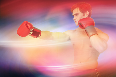 Muscly man wearing red boxing gloves and punching against purple skyの写真素材