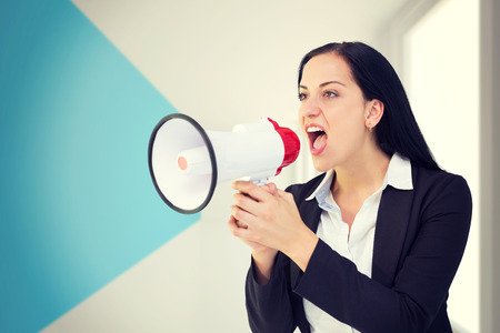 Pretty businesswoman shouting with megaphone against modern blue and white roomの写真素材