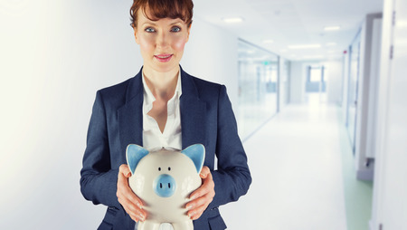 Businesswoman showing piggy bank against college hallwayの写真素材