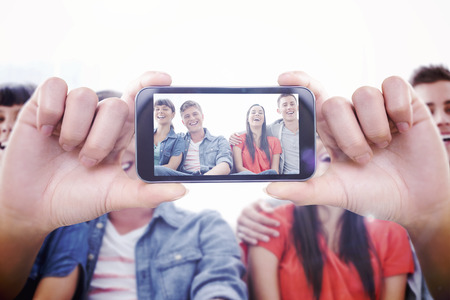 Hand holding smartphone showing against a group of laughing friends look into the camera