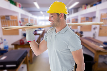 Worker with plank of wood against workshopの写真素材