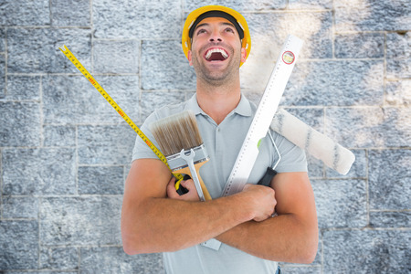 Laughing manual worker holding various tools against grey