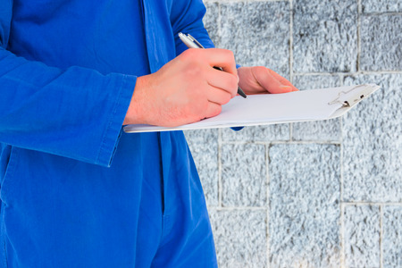 Male mechanic writing on clipboard against greyの写真素材