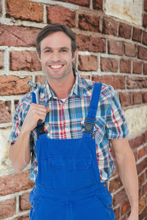 Confident plumber holding tool over white background against red brick wallの写真素材