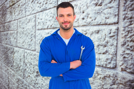 Happy mechanic holding spanner on white background against grey brick wallの写真素材