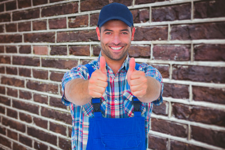 Portrait of happy male repairman gesturing thumbs up against red brick wall