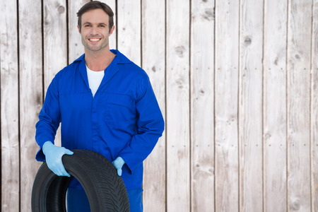 Confident mechanic holding tire against digitally generated grey wooden planksの写真素材
