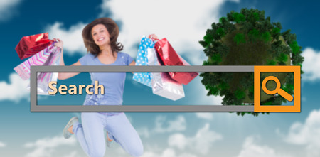 Excited brunette jumping while holding shopping bags against blue skyの写真素材