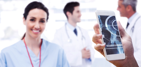 hand holding smartphone against nurse smiling at camera while doctors are talking together
