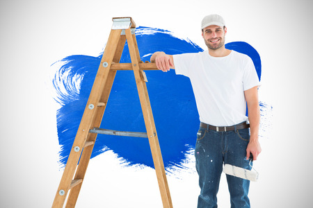 Happy man with paint roller standing by ladder against blue paintの写真素材