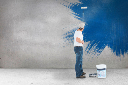Man using paint roller on white background against grey roomの写真素材