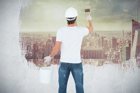 Rear view of man using paintbrush against room with large window looking on cityの写真素材