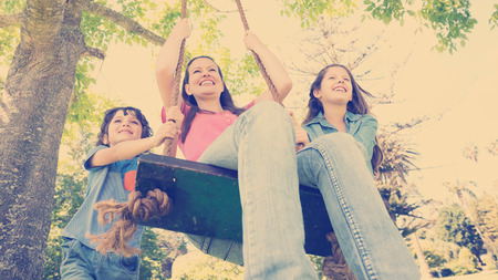Low angle view of kids pushing mother on swing in playgroundの写真素材
