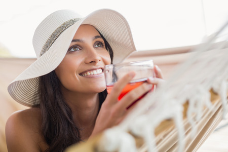 Pretty brunette relaxing on a hammock and drinking cocktail in patioの写真素材