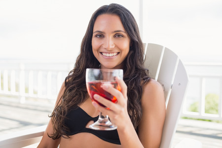 Pretty brunette sitting on a chair and drinking cocktail in patioの写真素材